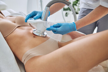 Beautiful elegant female in white bathrobe with perfect body getting anti-fat therapy in beauty salon