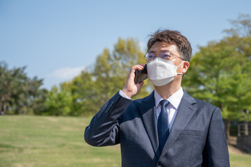 Fototapeta premium Middle-aged Asian businessman wearing a mask and using a smartphone on the lawn.
