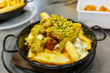 Porzione di patatine fritte con pesto di pistacchio, polpettine fritte, formaggio fuso e granella di pistacchio