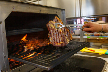 Bistecche di carne in cottura a fuoco vivo in un forno-brace di una braceria