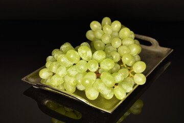 Ripe bunch of grapes on a metal tray, close-up, isolated on black.