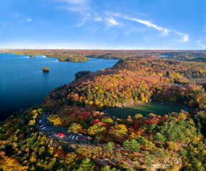 Aerial view of colorful fall forest by the fresh water lake - bright yellow, red, orange, green  trees. Blue sky, sunny day. Lion's Lookout, Muskoka, Northern Ontario, Canada.