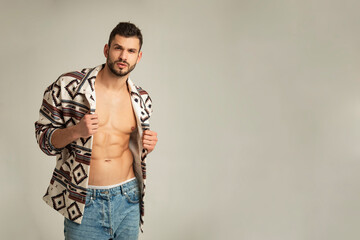 Fototapeta na wymiar Muscle strong beautiful stripped male model shirtless in denim jeans and etno jacket on grayisolated font background