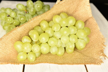 A ripe bunch of sweet grapes with a jute napkin on a wooden table, close-up.