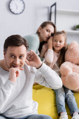Smiling man listening near wife and daughter with soft toy on blurred background.
