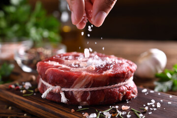 Hand sprinkling salt on fresh raw beef meat on a cutting board