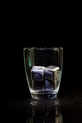 stainless steel cubes simulating ice in whisky glass on a black table.