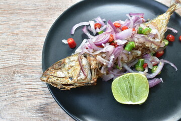 deep fried salty mackerel fish topping chop shallot and chili with slice lemon on plate