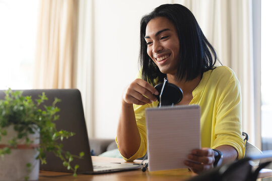 Happy mixed race transgender woman making video call using laptop, smiling, holding notes