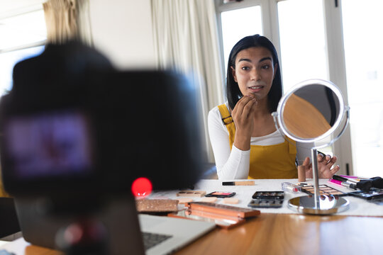 Mixed race transgender woman making vlog using laptop and camera putting on makeup - Powered by Adobe
