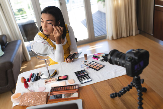 Happy mixed race transgender woman making vlog using laptop and camera putting on makeup