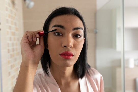 Portrait of mixed race transgender woman reflected in bathroom mirror putting on mascara