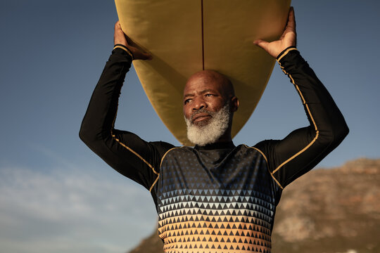 Senior african american man carrying surf board on his head on the beach
