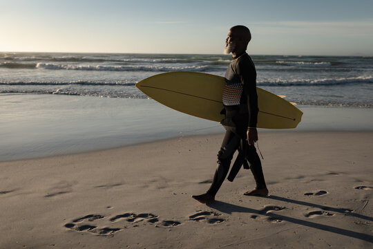 Senior african american man carrying surf board walking on the beach