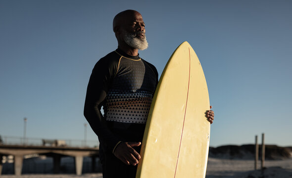 Senior african american man holding surf board standing on the beach