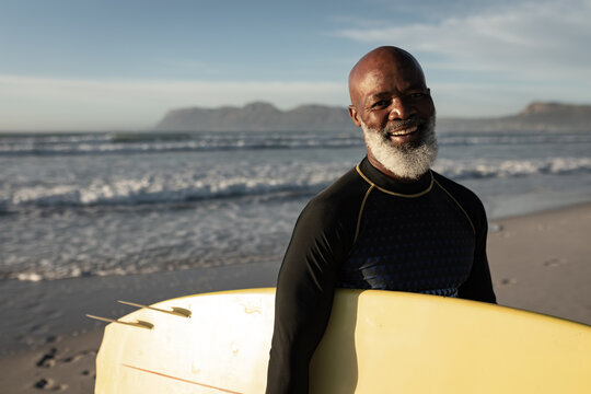 Portrait of senior african american man holding surf board smiling at the beach