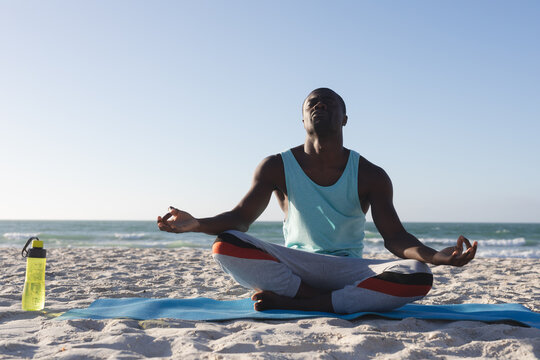 African american man exercising outdoors, practicing yoga, meditating on beach