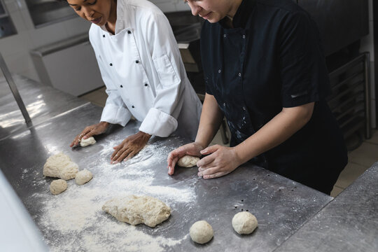 Mixed race professional chefs preapring dough on countertop covered with flour
