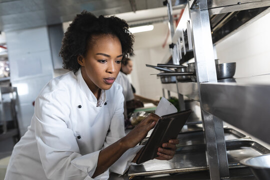 Mixed race professional chef looking at tablet with colleague in background