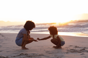 African american mother and daughter collecting shells at the beach smiling