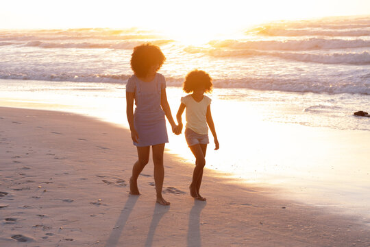 African american mother and daughter walking and holding hands at the beach