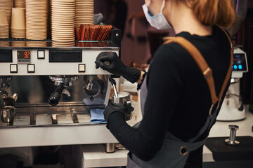 Young woman in barista uniform operating a coffee machine