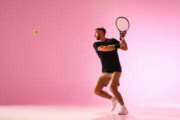 Young caucasian man playing tennis isolated on pink studio background, action and motion concept