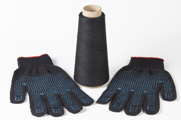 Close-up of a bobbin with black cotton thread and two black construction gloves on a white isolated background.