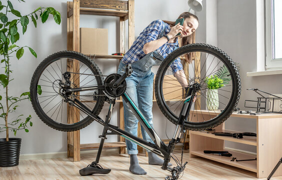 Woman is fixing a bicycle and using her phone. Concept of maintenance and preparation of the bike for the new season