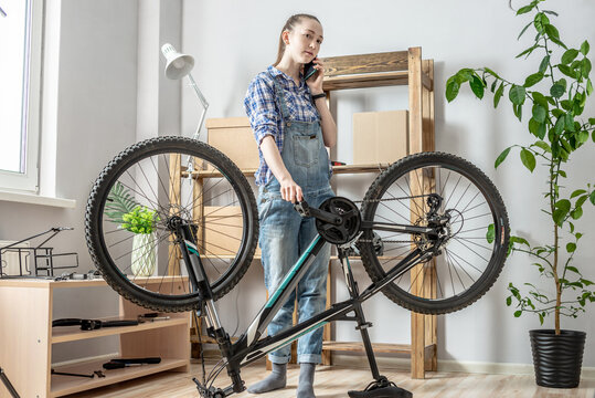 Woman is fixing a bicycle and using her phone. Concept of maintenance and preparation of the bike for the new season