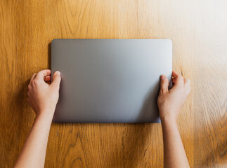 Mujer joven cogiendo un ordenador portátil de color plateado oscuro con las dos manos sobre una...