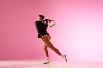 Young caucasian man playing tennis isolated on pink studio background, action and motion concept