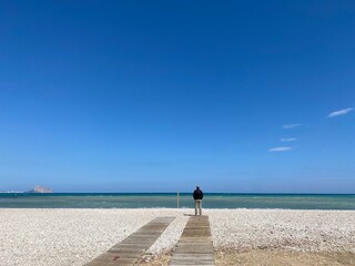 A young man stands at the deserted beach of Albir-Spain.