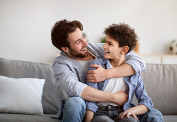 Two generations concept. Happy father embracing son, looking at each other and smiling, sitting on...