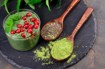 Matcha green tea chia seed pudding, dessert with fresh mint, berry and coconut on a black slate background