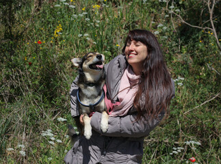 Naklejka na ściany i meble Smiling female portrait with smiling dog in her arms, surrounded by nature and spring flowers