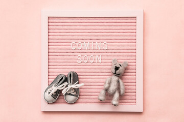 Waiting for labour, maternity concept. Coming soon words on pink frame with baby shoes and teddy...