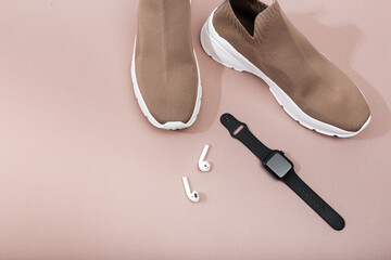 modern beige sneakers with smart watch and earplugs on beige background  - Image