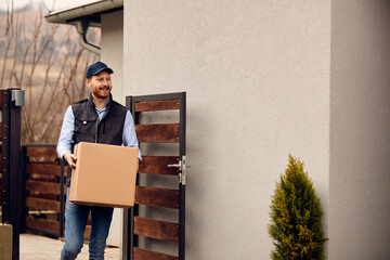 Smiling delivery man carrying cardboard box and delivering package to customer's home.