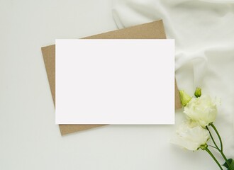Wedding stationery mockup, empty greeting card, invitation for text or design, flat lay with brown envelope, white flowers and silk scarf.