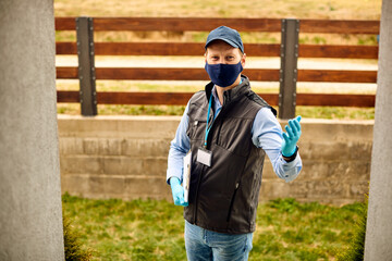 Smiling male courier wearing protective face mask  and gloves during home delivery due to COVID-19 pandemic.