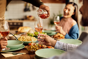 Close-up of man serving wine to his friends during lunch at home.