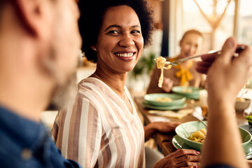 Happy African American woman being fed by her husband at dining table.