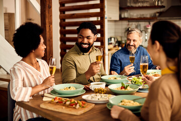 Happy black man drinking wine and enjoying in lunch with his friends at dining table.