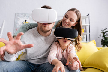 Excited child and father using vr headsets near smiling mother.