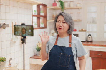 Close up of camera recording pensioner mature woman cooking and making video live for the social media platform. Senior retired influencer woman creating online content video in her kitchen at home.