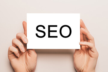 Female hands hold card paper with text SEO on a yellow background. Business and finance concept