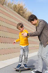 Father is teaching his son to ride a skateboard, outdoors
