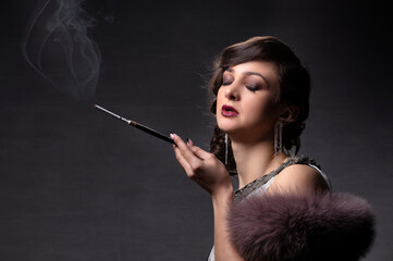 Obraz premium Retro woman portrait. A beautiful woman in the style of the 20s and 30s with a cigarette holder smokes.