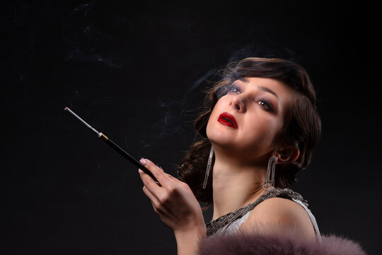 Retro woman portrait. A beautiful woman in the style of the 20s and 30s with a cigarette holder smokes.